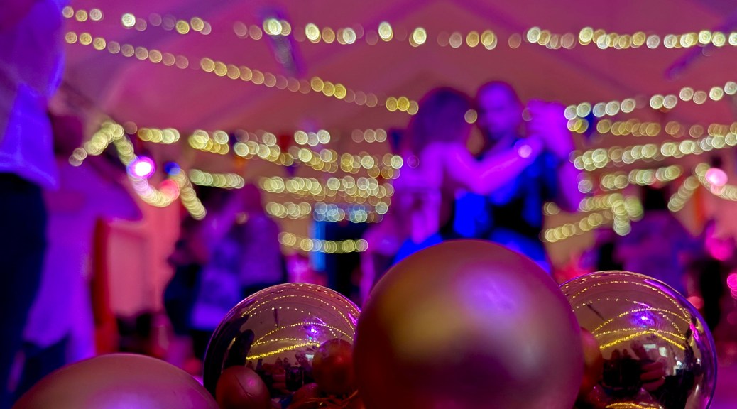A close-up of golden xmas decorations with an out-of-focus view of the colourful hall behind